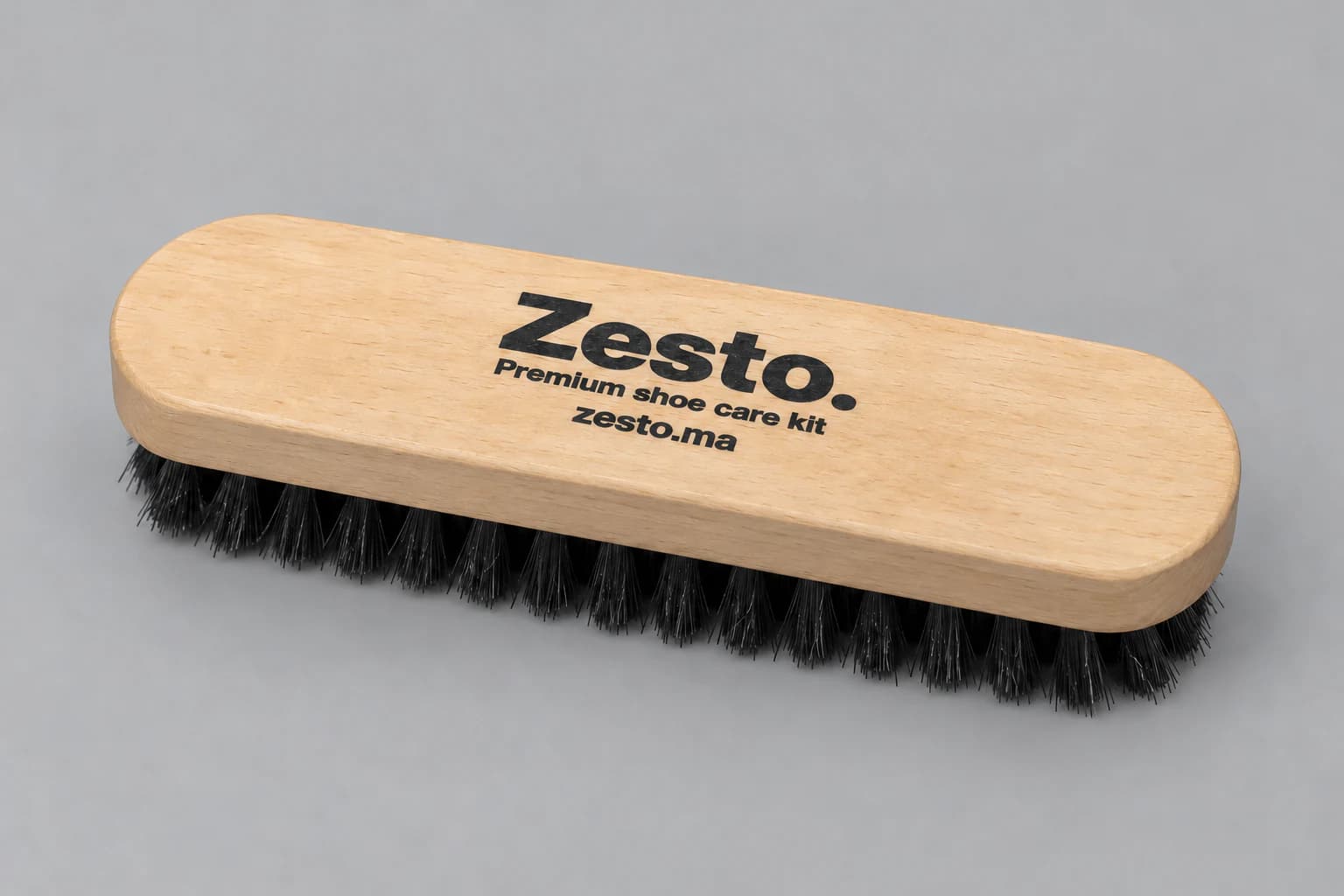 Brosse Zesto. en bois clair avec marquage noir sur le dessus et poils noirs uniquement dessous, sur fond gris clair.