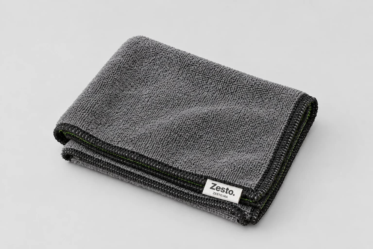 Microfibre grise Zesto. pliée avec bord noir et couture intérieure verte, sur fond gris clair.
